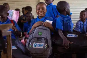 Niño refugiado sudanés sujeta una mochila donada por Plan International en un campo para desplazados en Chad