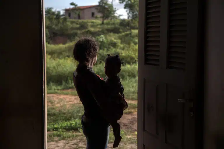 Una madre adolescente mira al horizonte mientras sostiene en brazos a su bebé en Brasil © Plan International / Natalia Moura