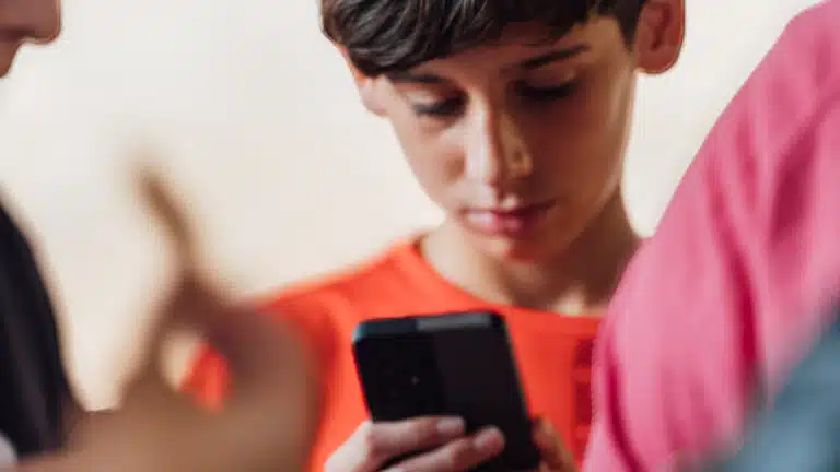 Un adolescente revisa su teléfono móvil junto a un grupo de amigos en Paiporta, Valencia. Febrero, 2026 © Antonio Portillo / Plan International