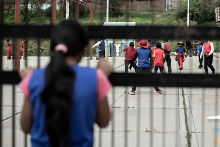 Una niña es forzada a mirar desde la barrera mientras un grupo niños juega al fútbol en Perú © Plan International